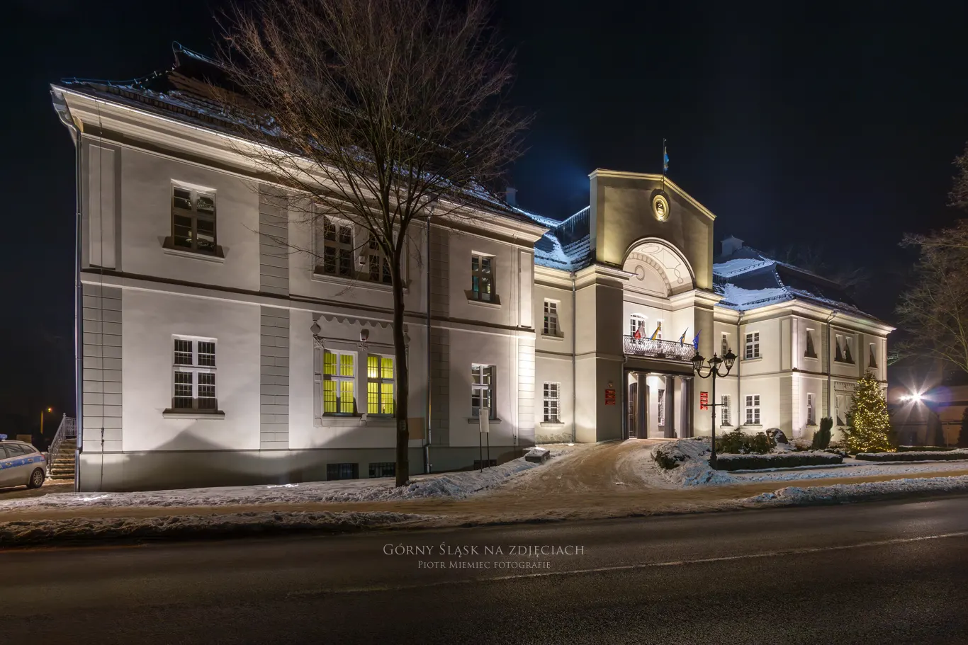 Pałac w Tworogu sfotografowany wieczorem, oświetlony subtelną iluminacją.